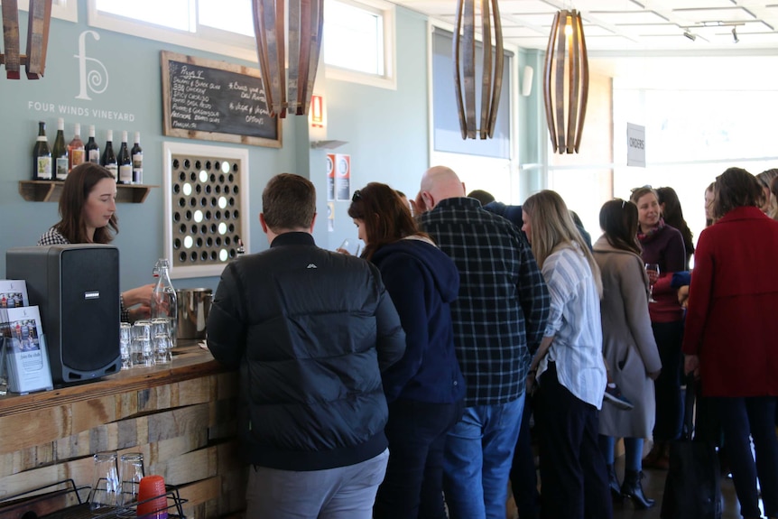 Lots of people stand around a bar, tasting wine.