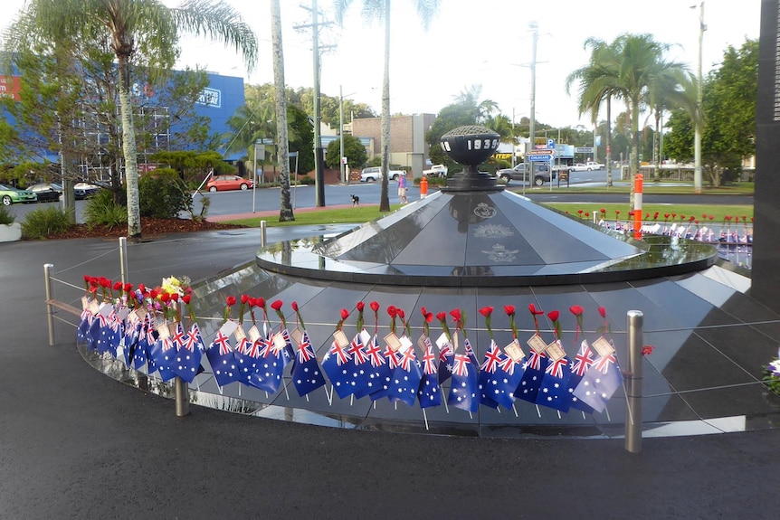 A round, black monument with small Australian flags and poppies decorating a rail in front of it.