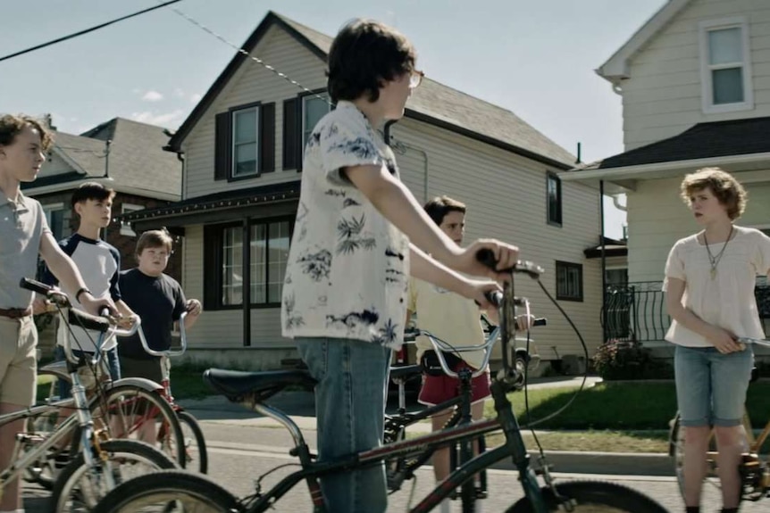 Still image from 2017 film IT of the protagonist group of Maine children on bicycles in a suburban setting.