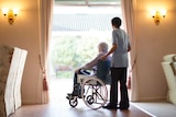 An aged care worker with a resident in wheelchair sitting at window.