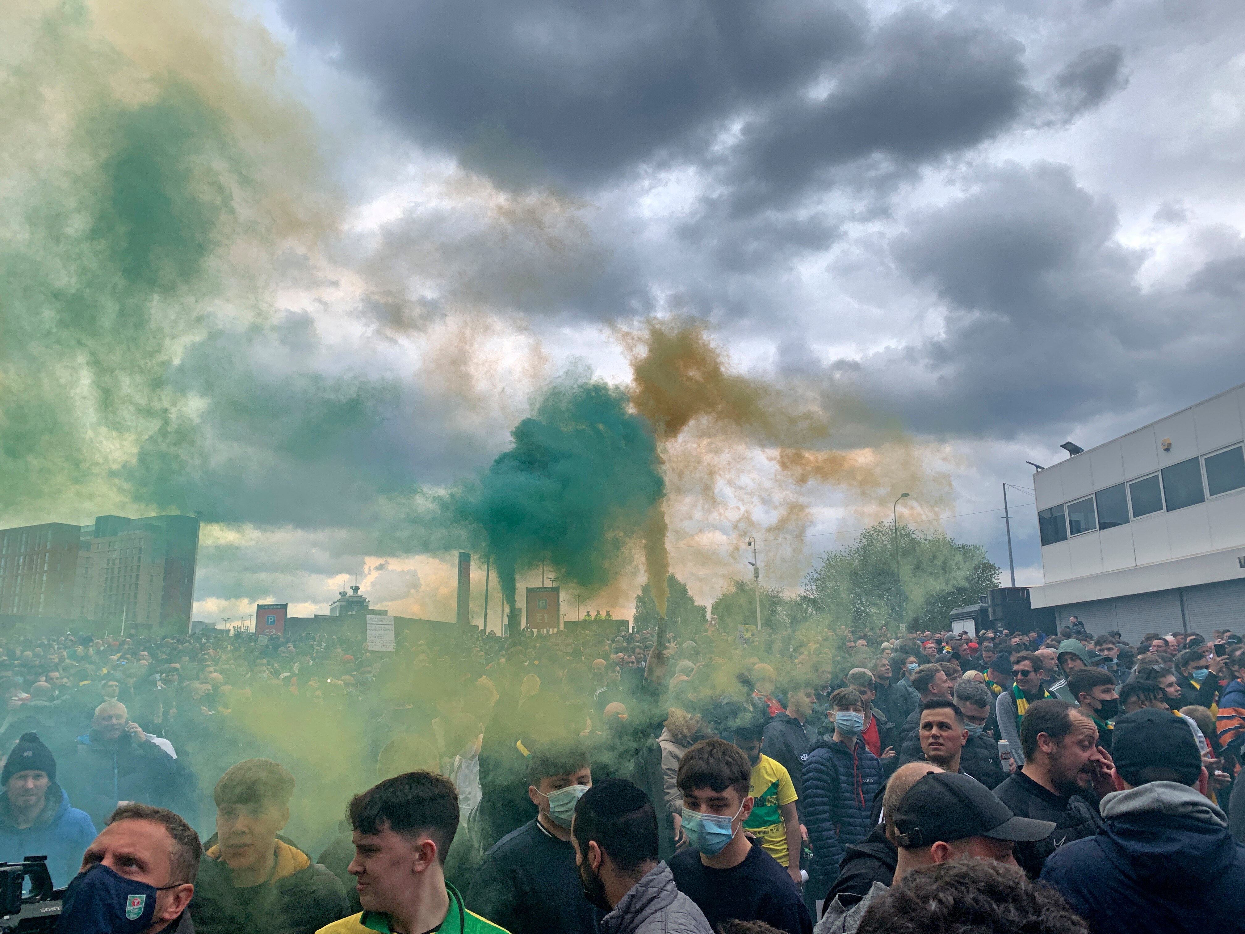 Green and yellow smoke hangs in the air as football fans hold flares outside their home ground.