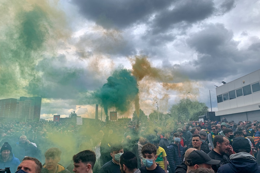 Green and yellow smoke hangs in the air as football fans hold flares outside their home ground.