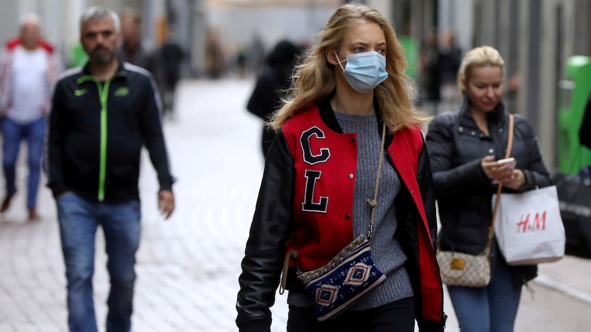 three people walk along a path in Amsterdam, with the woman in front wearing a face mask