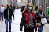 three people walk along a path in Amsterdam, with the woman in front wearing a face mask
