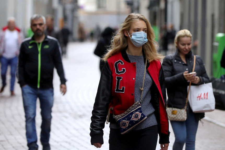 three people walk along a path in Amsterdam, with the woman in front wearing a face mask