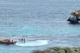 People stand on a reef near a boat, as a helicopter lands on a nearby rocky outcrop.