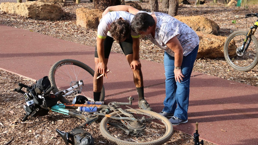 Declan von Dietze hunches over next to his mountain bike with his hands on his knees and his mum alongside him.