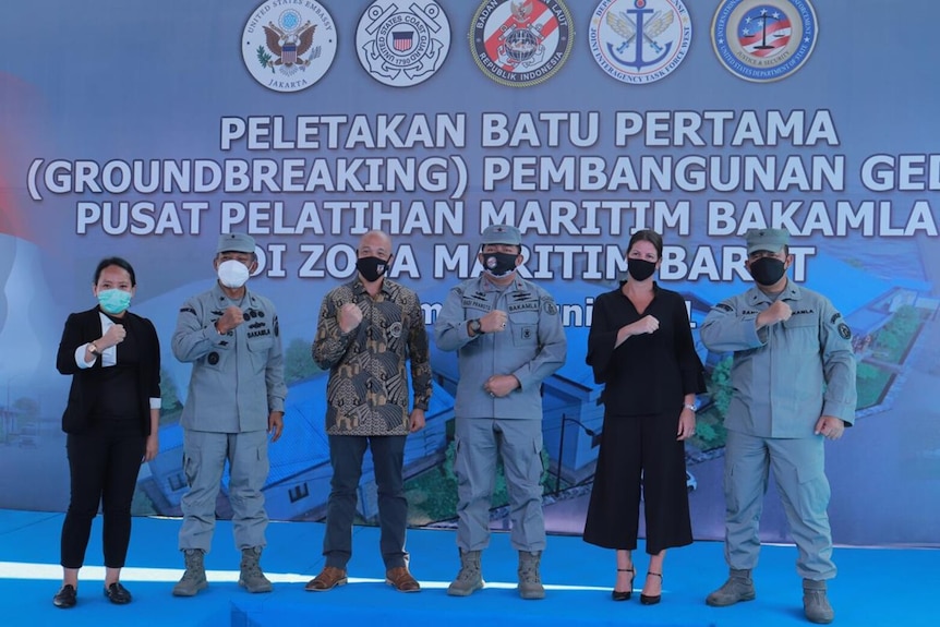 Men and women pose for a photo in front of an image that includes the US Coast Guard emblem.