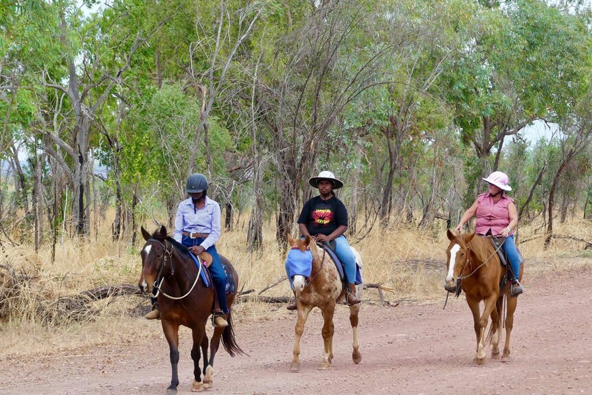 Three riders on horses walking down gravel road