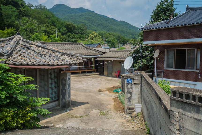 Low houses sit in the foreground in front of green hills.