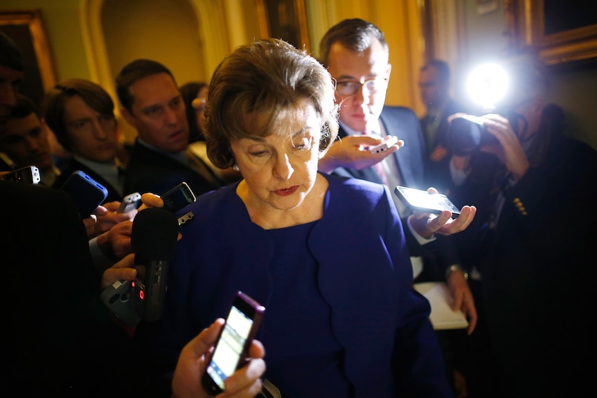 A woman in a purple suit surrounded by reporters holding recording devices