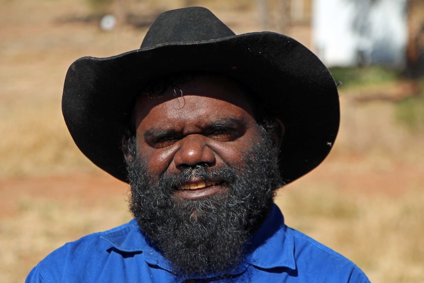 A man in a broadbrim hat and blue shirt smiling outside