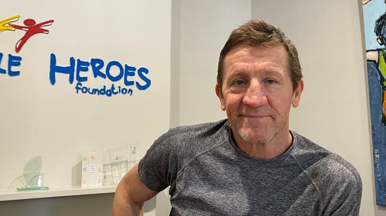 Chris McDermott stands in front of a white wall with Little Heroes Foundation written on it