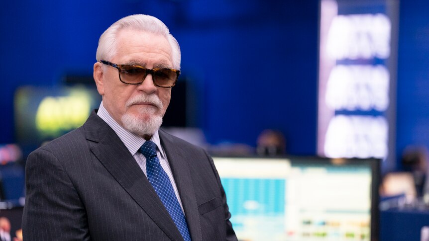 A production still of Logan in wearing sunglasses in the newsroom.
