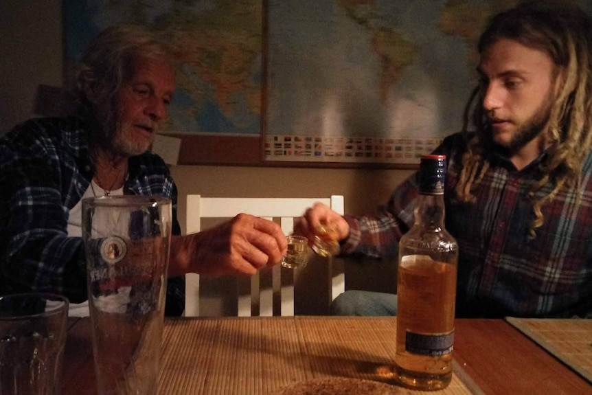 an older man does a shot next to a younger man in a bar