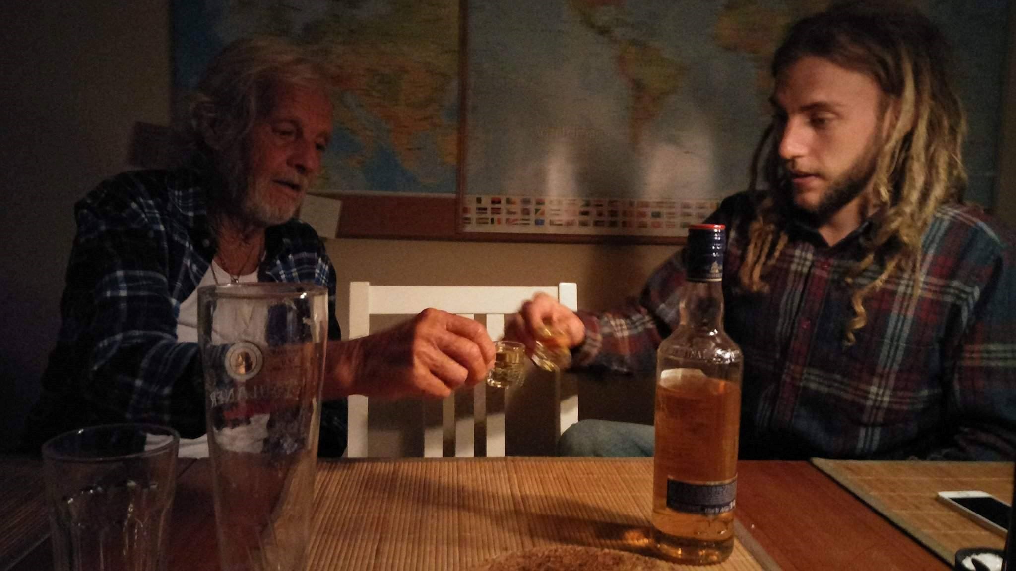 an older man does a shot next to a younger man in a bar