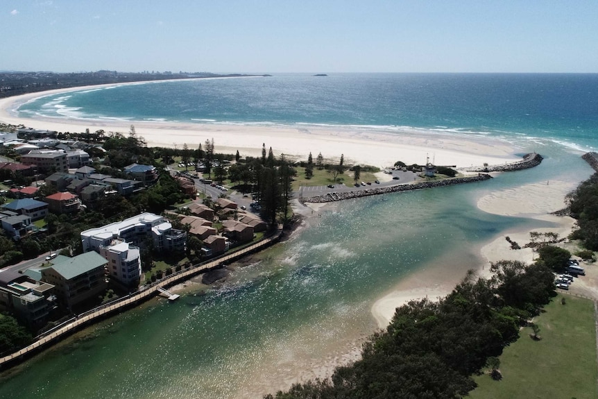 An drone photo of a creek mouth and ocean, surrounded by houses and buildings.