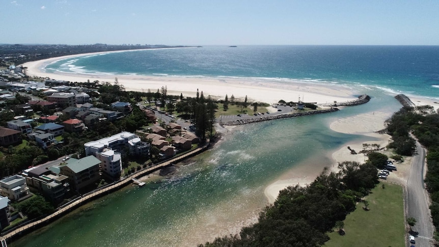 An aerial view overlooking a small town next to a river inlet that leads out to a beach.