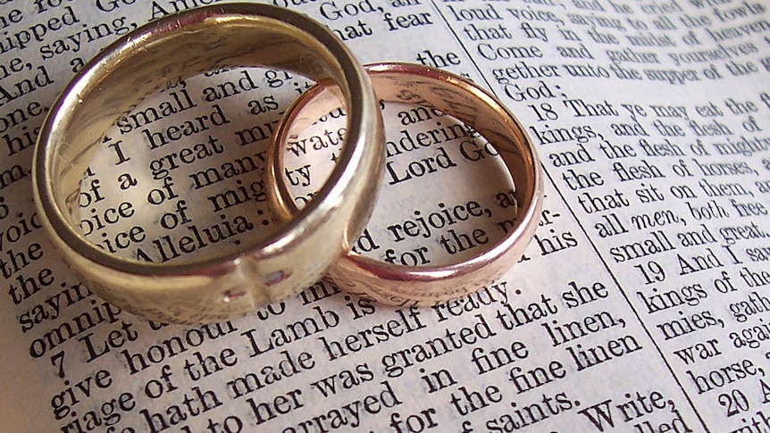 A pair of wedding rings sit on a Bible.