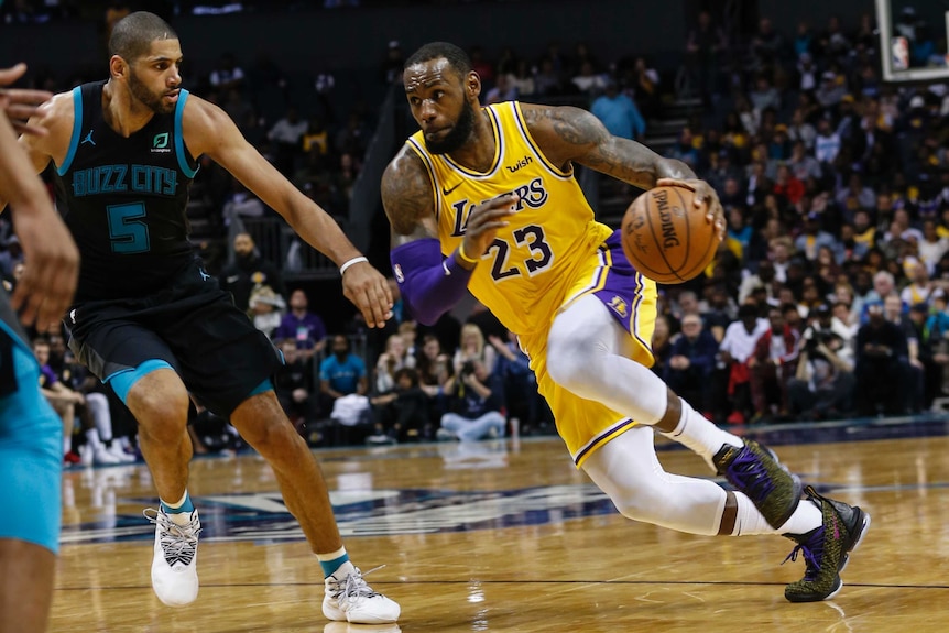 LeBron James takes the ball in his left hand and drives towards the basket with another player in dark blue watching him