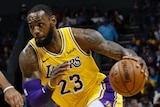 LeBron James takes the ball in his left hand and drives towards the basket with another player in dark blue watching him