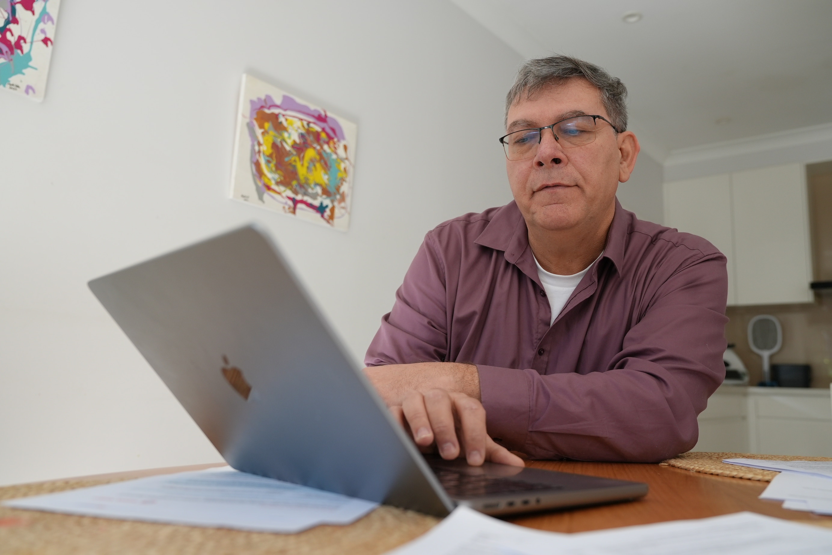 A man with a purple shirt and glasses reading over documents on his laptop