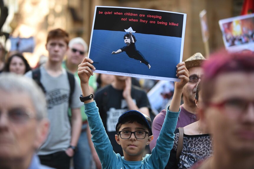 A young protester holds up a placard in support of migrant refugees at a rally in Sydney