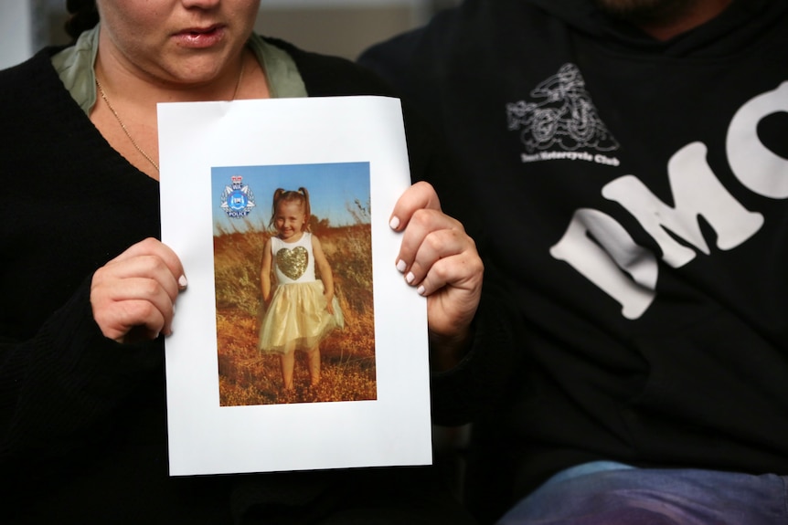 A woman holds up a poster of a little girl.