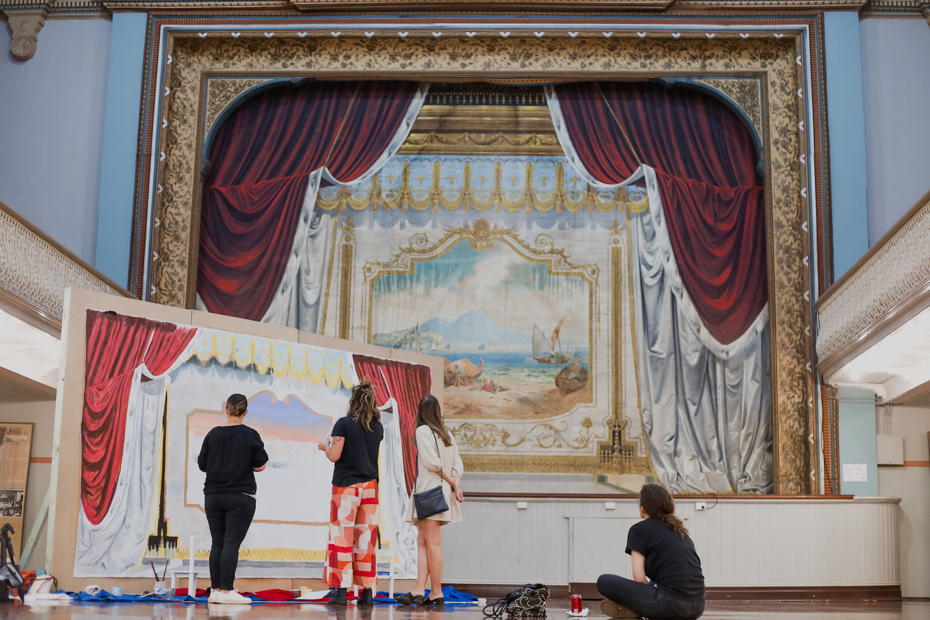 People stand before an artwork featuring red curtains in front of an even larger artwork of red curtains.