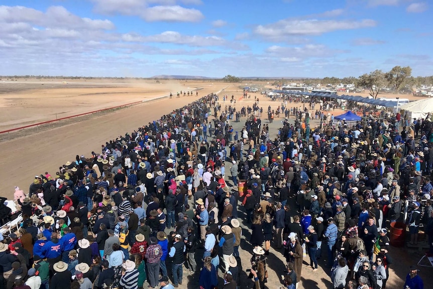 An aerial view of a crowd of people standing next to a dusty race track.