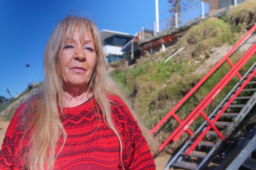 Woman wearing red sweater stands on beach in front of red stair case