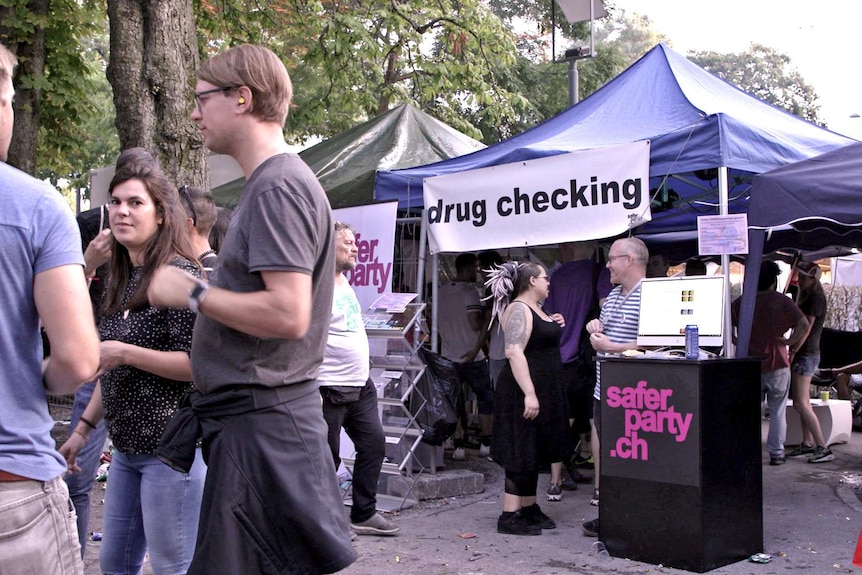 A marquee has a banner in front of it with the words 'drug checking' in a street