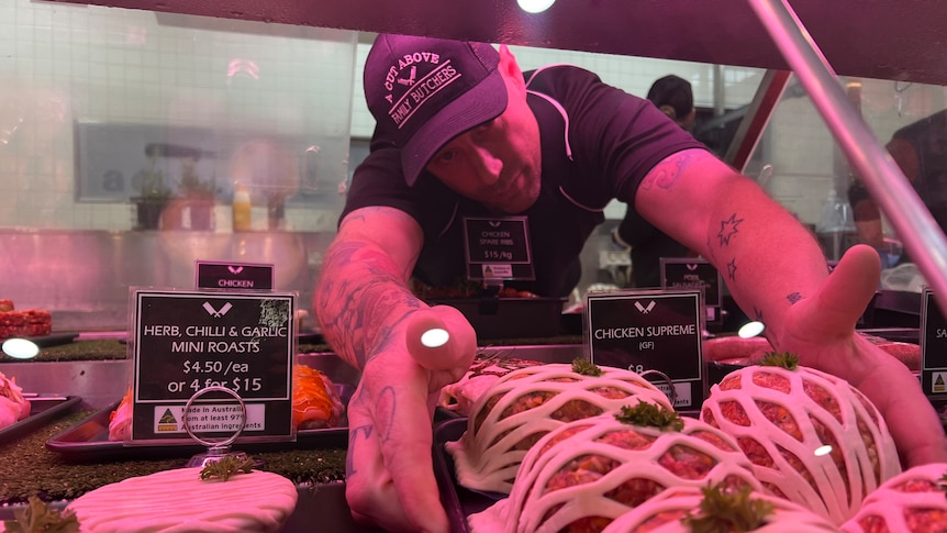 A butcher places a tray of meat in a display cabinet 