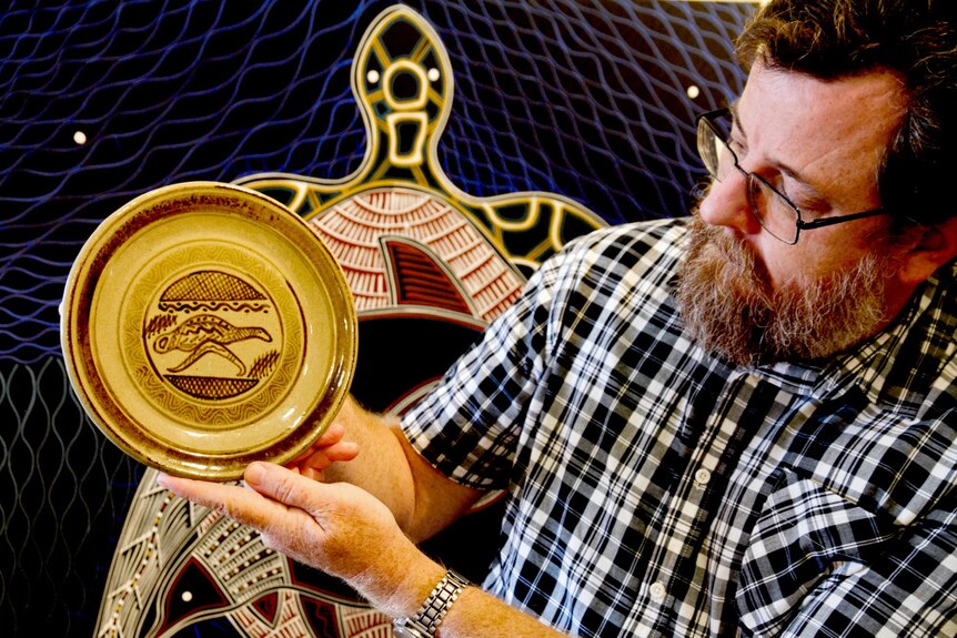 Exhibition co-curator Mathew Wengert hold up a dinner plate covered in Indigenous designs.