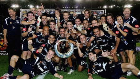 Melbourne Victory players celebrate the grand final win around the trophy