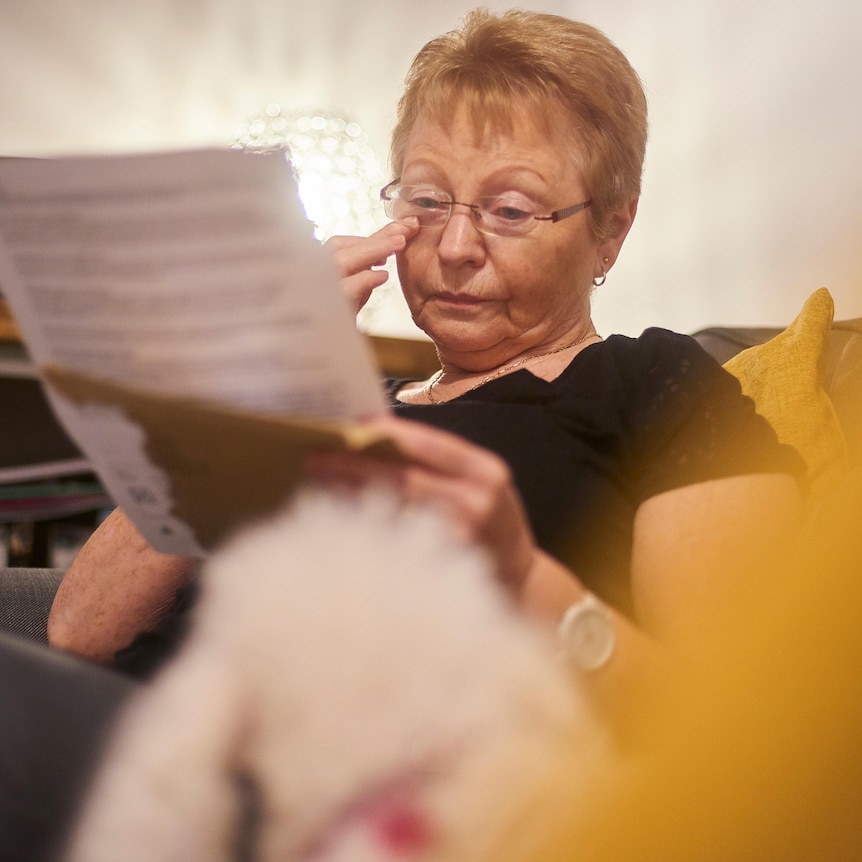 older woman wearing glasses in a chair reading a letter who appears upset
