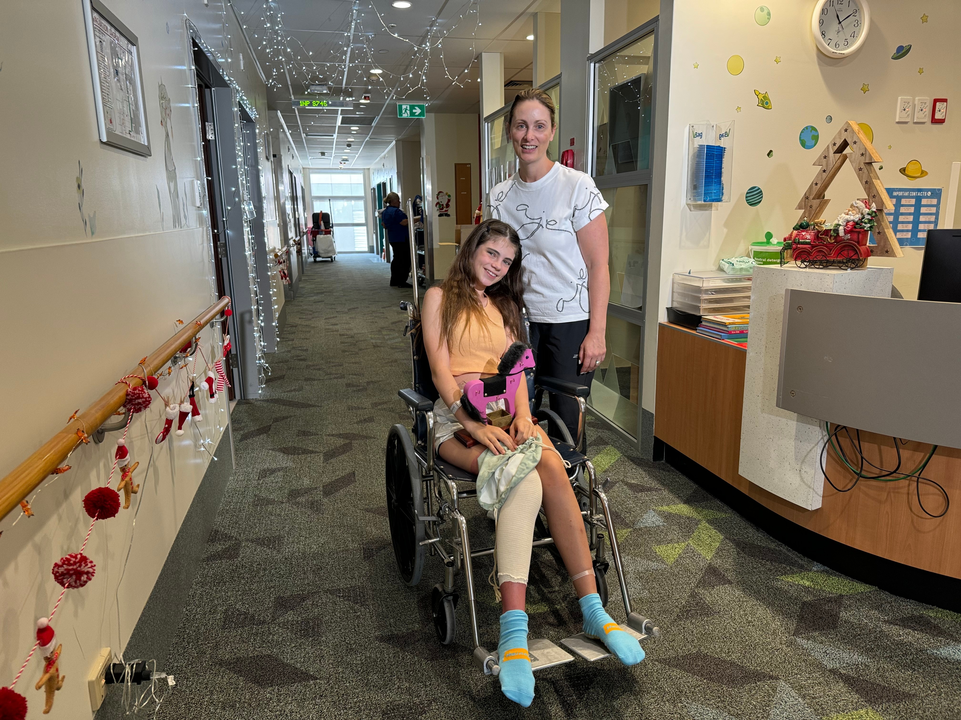 A girl in a wheelchair smiles while her mum stands next to her