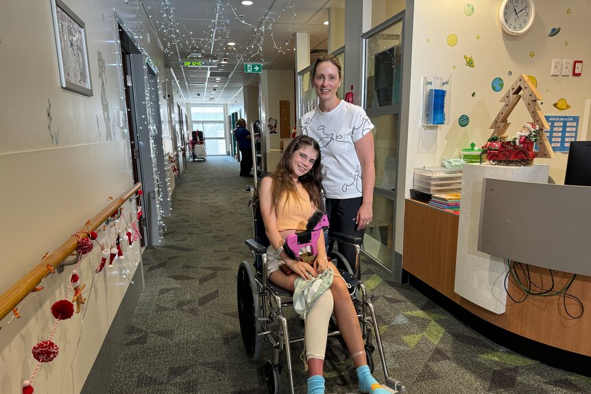 A girl in a wheelchair smiles while her mum stands next to her