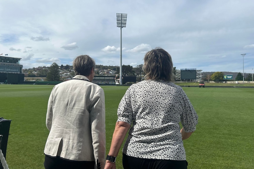 Two women walk onto a cricket ground.