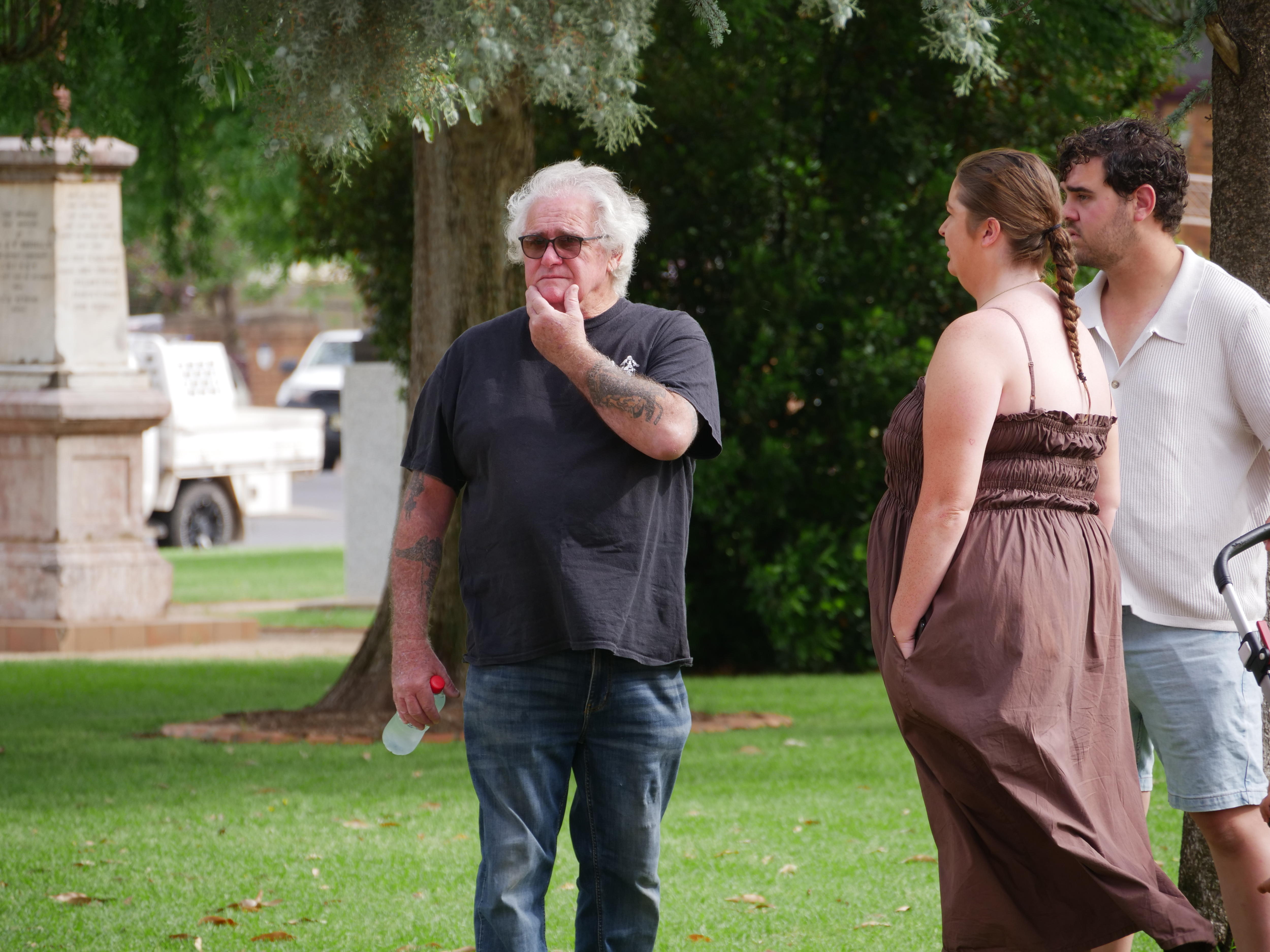 A man in a black t-shirt and sunglasses with his hand on his chin.