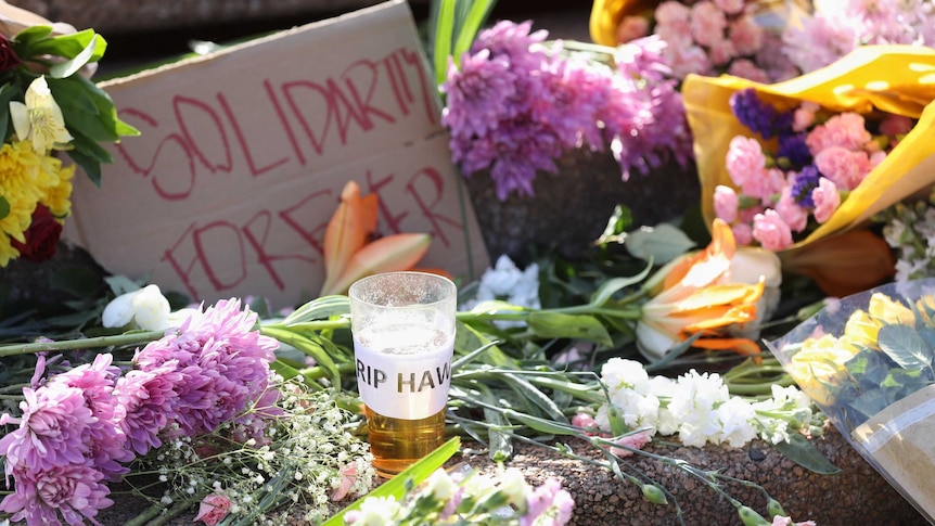 A beer with "RIP Hawkey"  and a "Solidarity forever" sign sit among flowers on Opera House steps