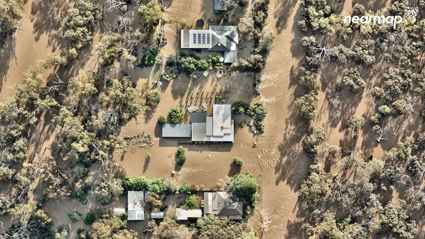Three homes alongside each other can be seen from above completely surrounded by brown floodwater 