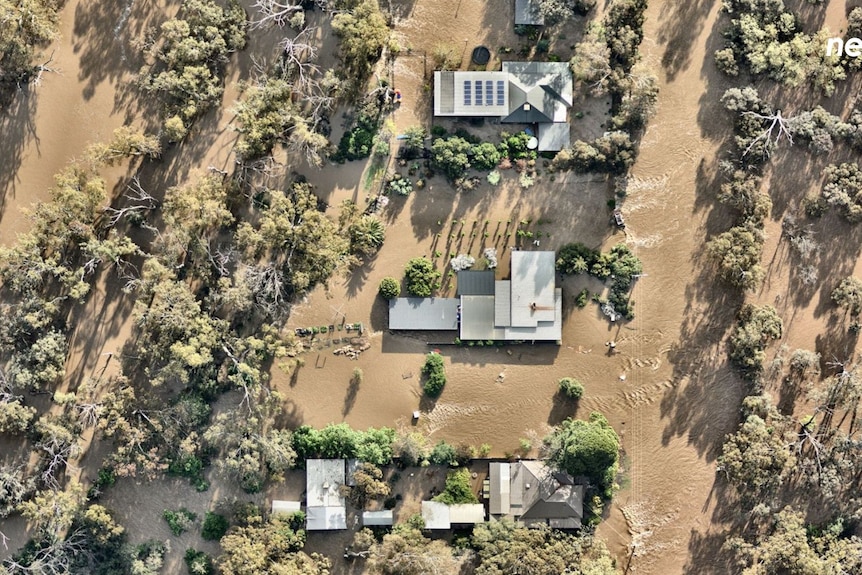 Three homes alongside each other can be seen from above completely surrounded by brown floodwater 