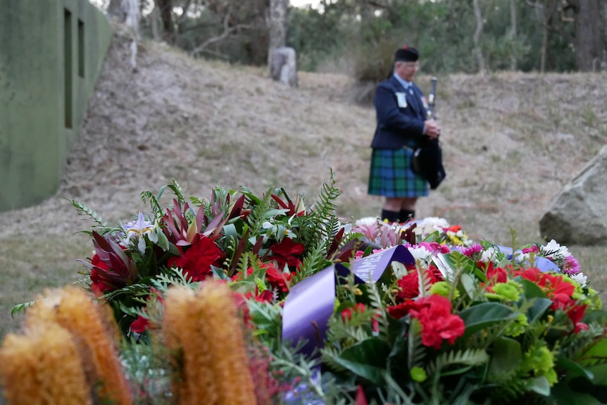Wreaths lay in the foreground with a musician and war bunker in the background.