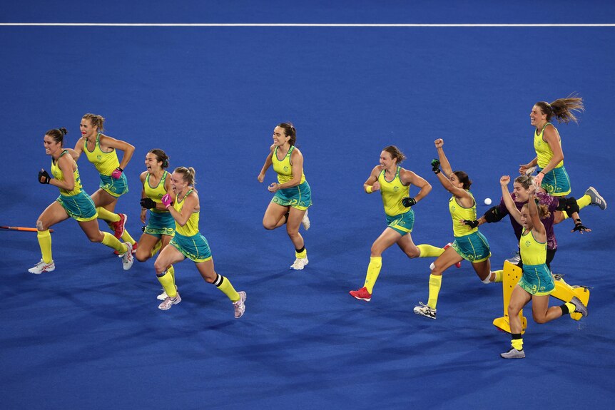 Australia players run forward with their arms in the air and smiles on their faces