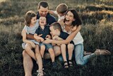 A photo of a family with four children sitting in the grass, all laughing wildly.