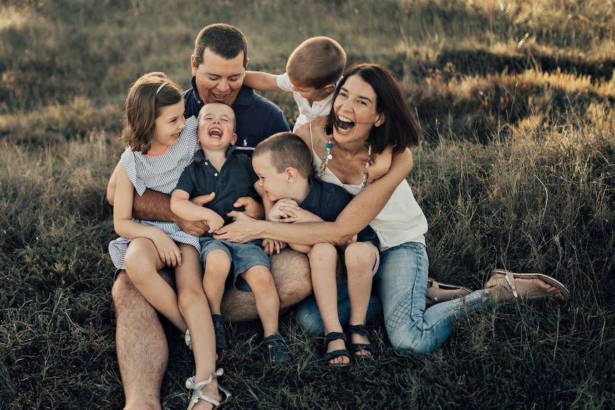 A photo of a family with four children sitting in the grass, all laughing wildly.