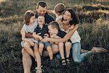A photo of a family with four children sitting in the grass, all laughing wildly.