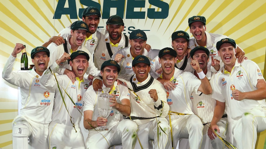 Australia's men's cricket team pose with a crystal urn-shaped and shout in front of a sign reading "THE ASHES".