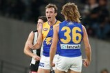 A West Coast AFL player shouts in celebration as a teammate stands in front of him after a goal.
